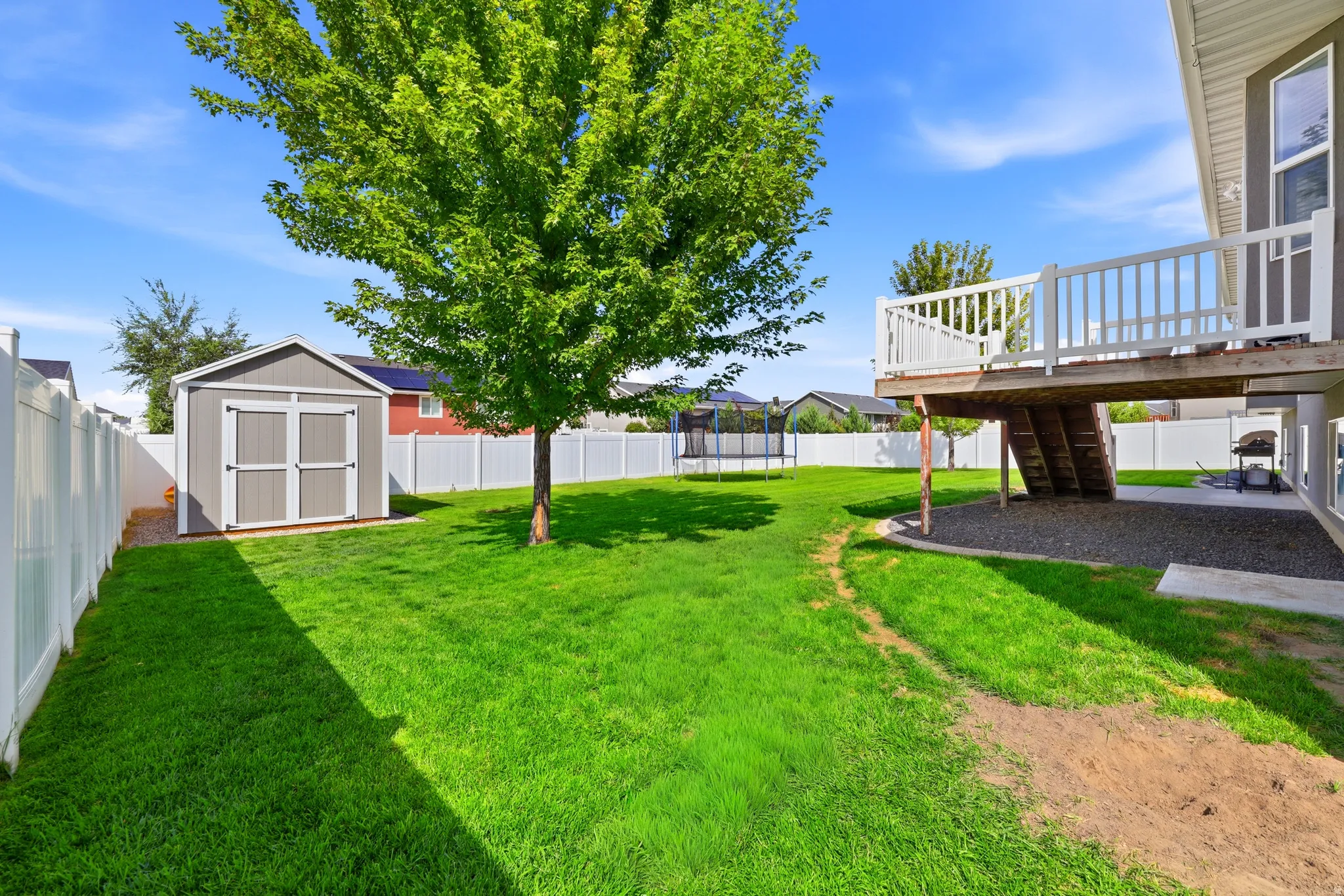 Expansive backyard featuring a manicured lawn, a detached storage shed, a raised deck with white railings, and a privacy fence