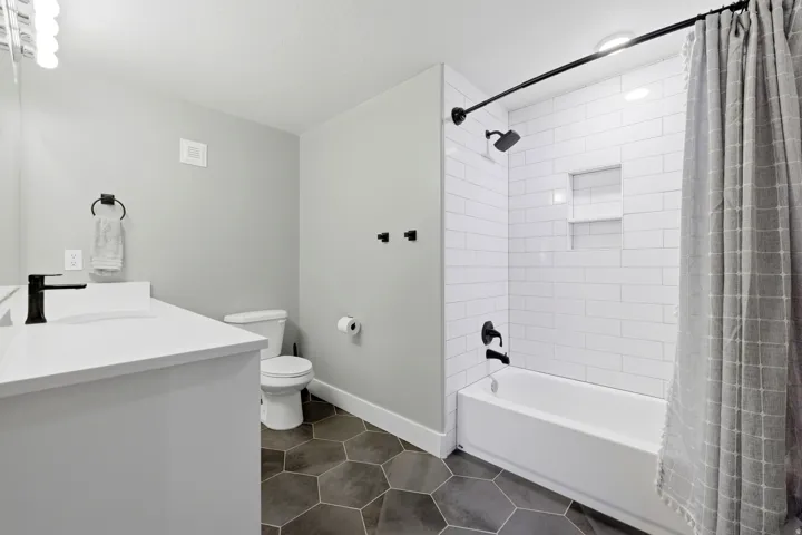 Bathroom featuring a white vanity with integrated sink, black fixtures, hexagon tile flooring, and a subway-tiled shower with recessed shelving