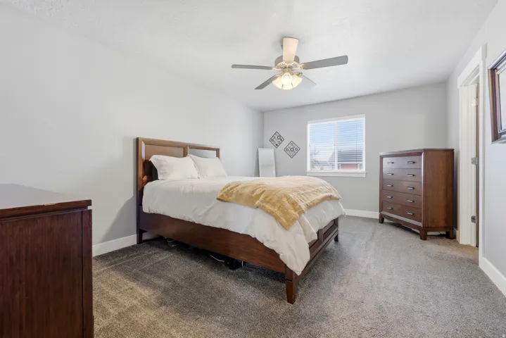 Neutral tone wall paint, light gray carpet, ceiling fan with integrated lighting, white trim, and a window with blinds