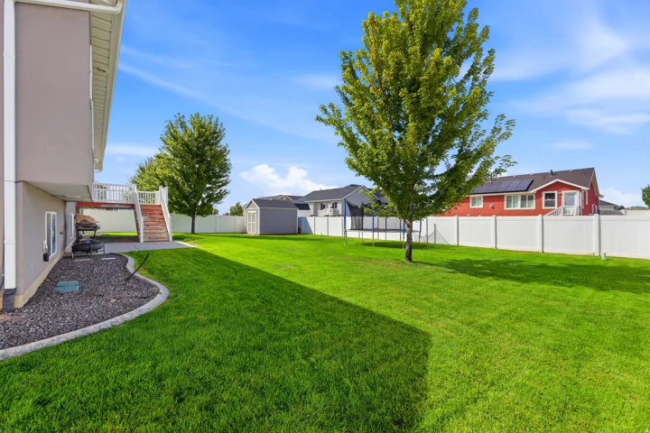 Expansive backyard featuring a manicured lawn, mature trees, white privacy fencing, a wood deck with stairs, and a detached shed