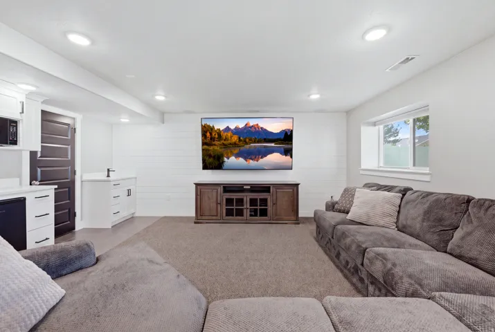 Recessed lighting, shiplap accent wall, built-in entertainment console, wet bar with white cabinetry, and a compact window