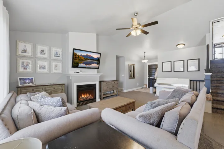 Living area featuring a ceiling fan, a fireplace with a white mantel, and a dark-toned door