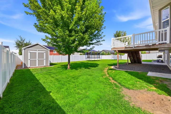 Expansive backyard featuring a manicured lawn, a detached storage shed, a raised deck with white railings, and a privacy fence