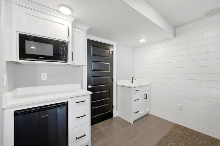 White cabinetry with dark hardware, built-in microwave, compact refrigerator, and a sink with a dark faucet