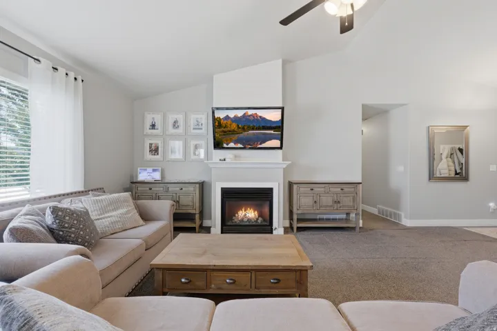 Vaulted ceiling with ceiling fan, gas fireplace with a white mantel, light-colored walls, and gray carpet flooring