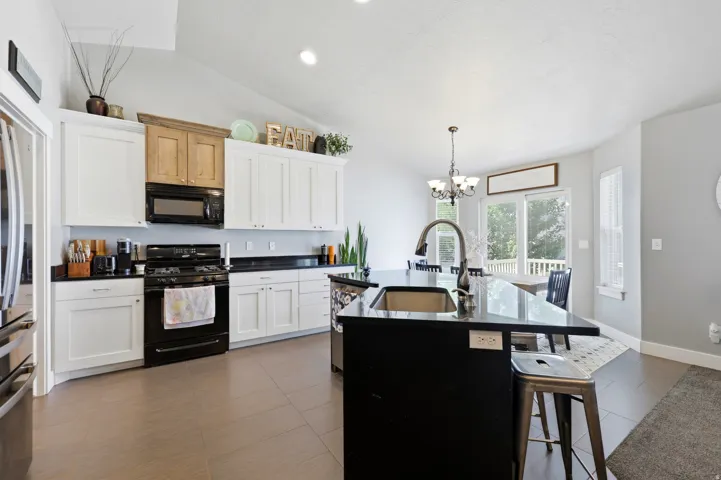 Kitchen featuring white cabinetry, black countertops, a central island with an integrated sink, stainless steel appliances, and tile flooring
