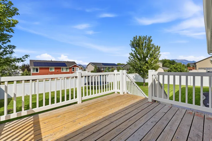 Expansive wood deck with white railings and stairs, overlooking a fenced yard with manicured lawn and mature trees