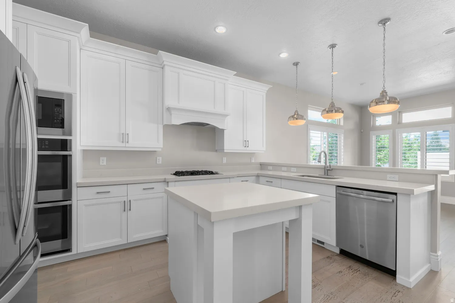 White shaker cabinetry with crown molding, light-toned countertops, a central island, stainless steel appliances, and wood-finish flooring