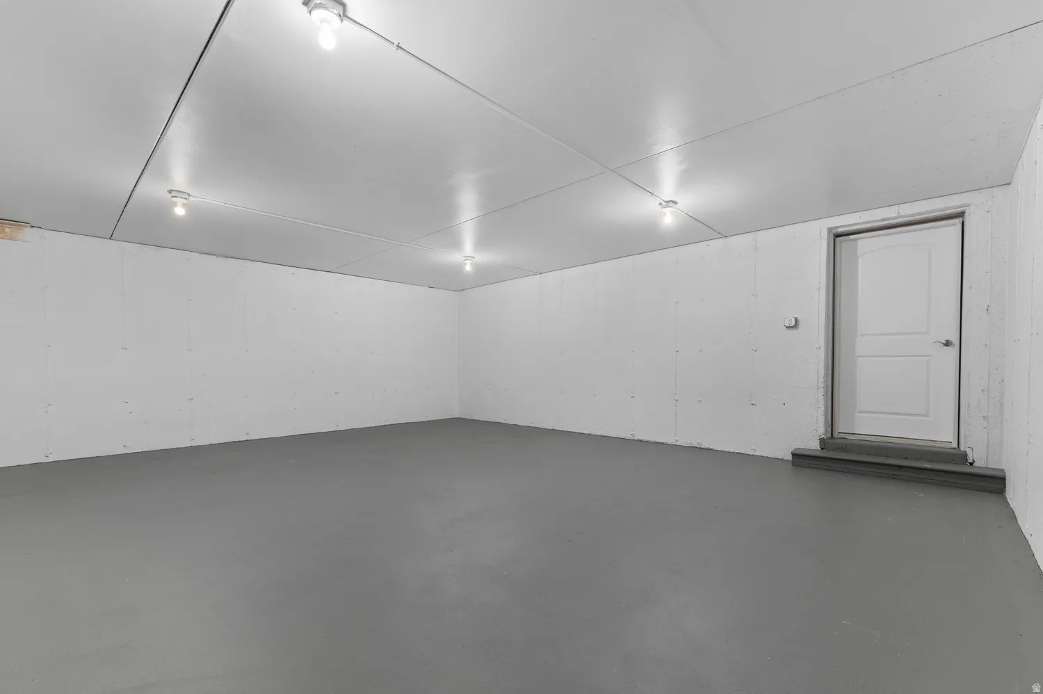Spacious room featuring a smooth gray floor, white concrete walls, and multiple ceiling-mounted light fixtures