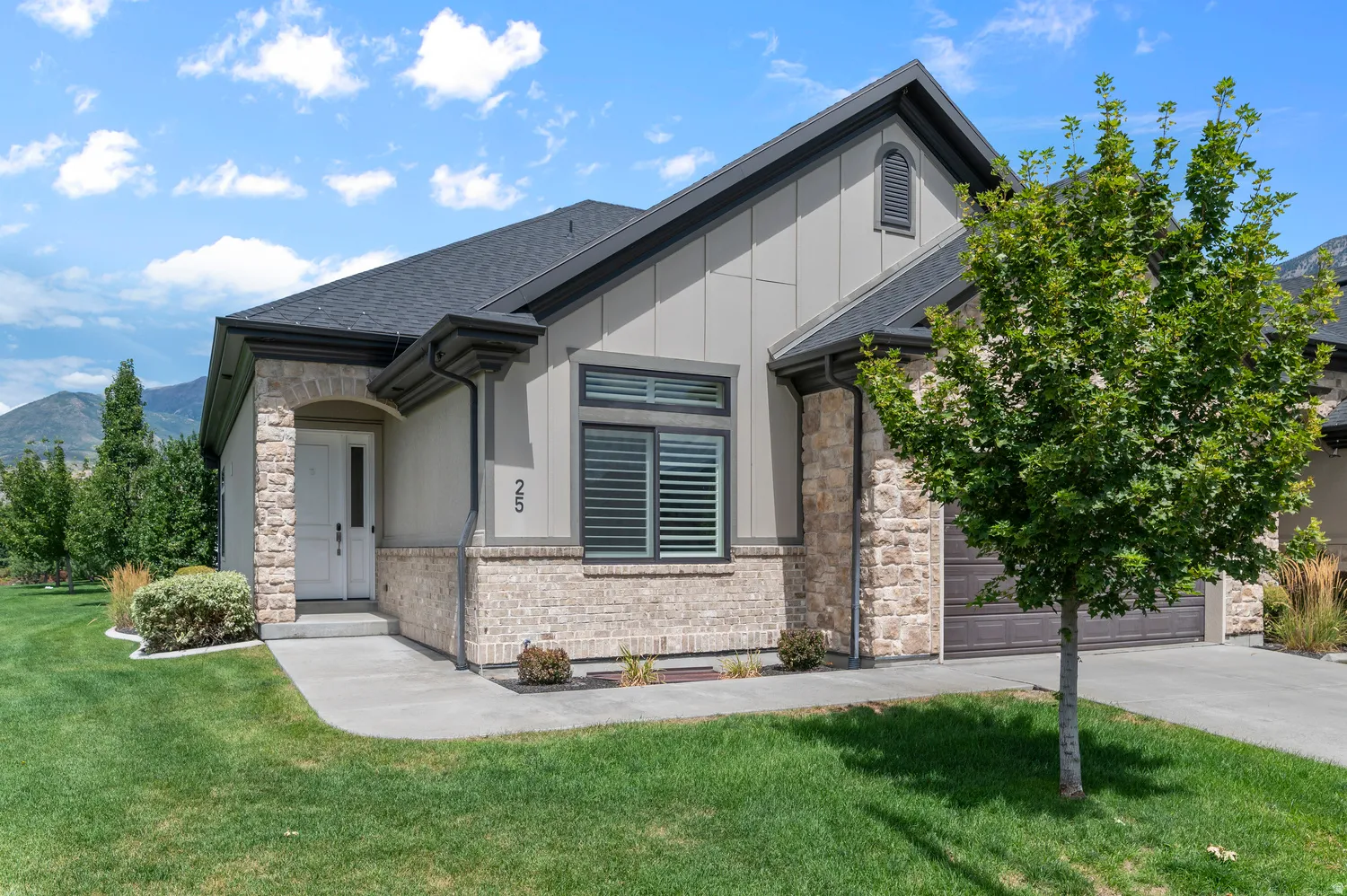 Exterior featuring stone and brick accents, a dark shingle roof, attached garage, and manicured lawn