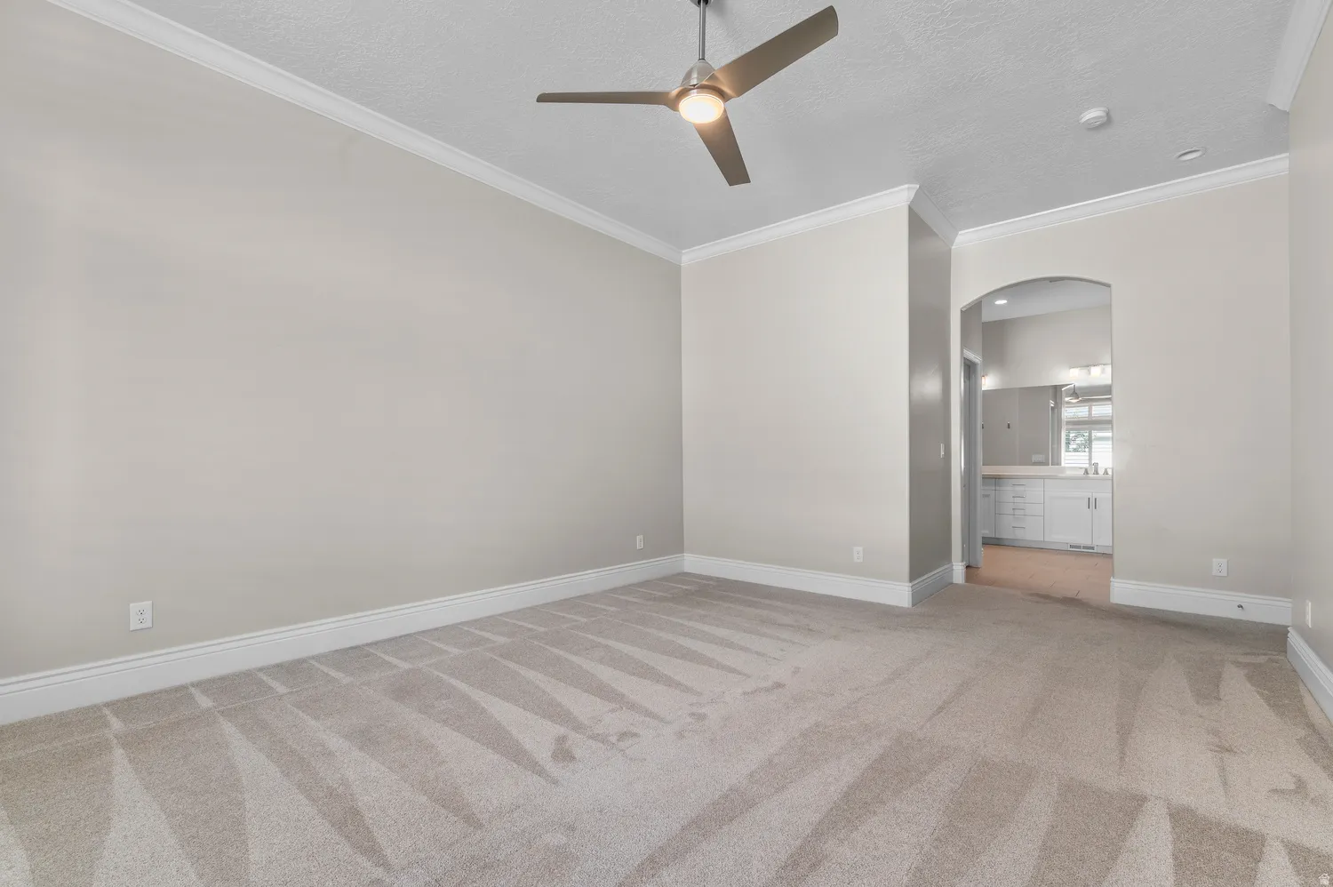 Spacious room with crown molding, textured ceiling, a ceiling fan, and arched entryway
