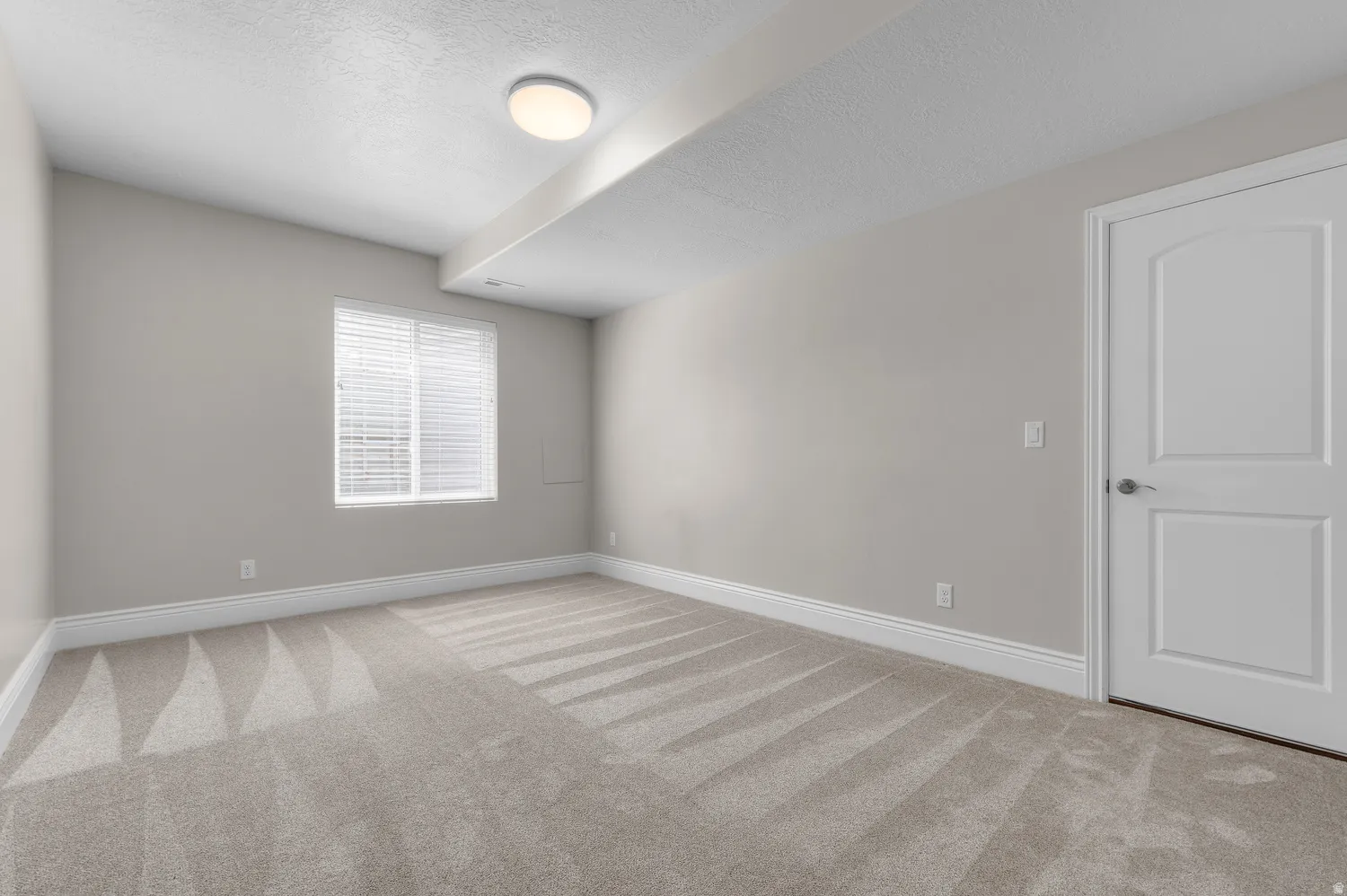 Neutral tone walls with white trim, light-colored carpeting, and a single window with blinds