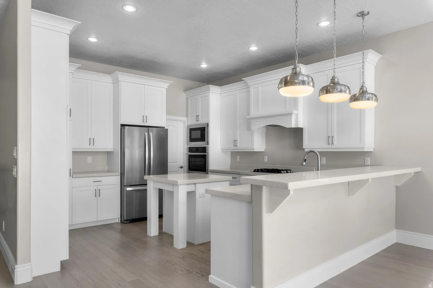 White shaker cabinetry, stainless steel appliances, light wood-finish flooring, recessed lighting, and a kitchen island with pendant lighting