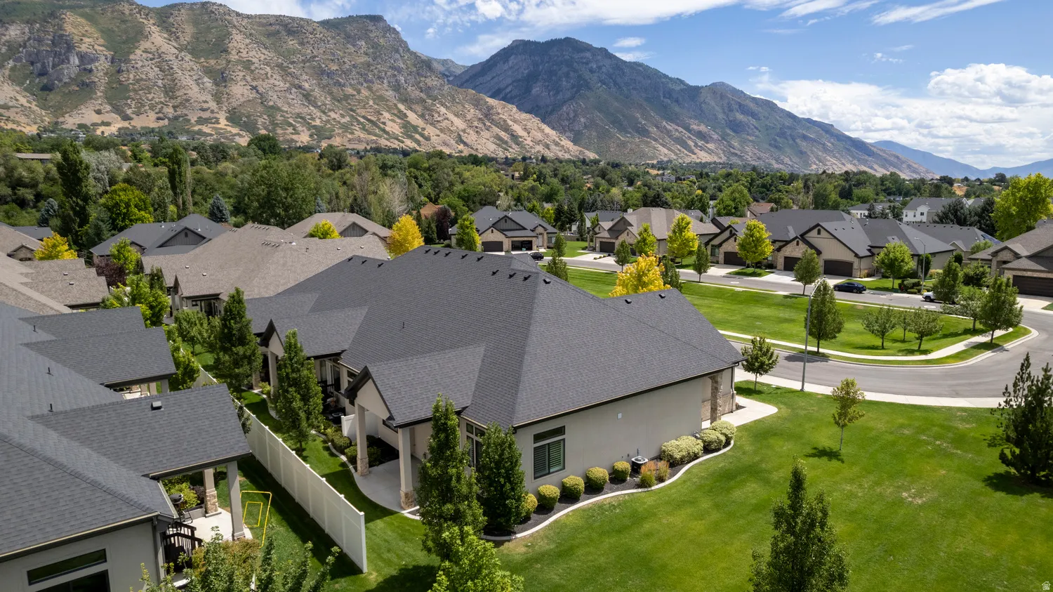 Expansive residential neighborhood with mountain scenery, featuring single-family homes with gray asphalt shingle roofs and manicured lawns