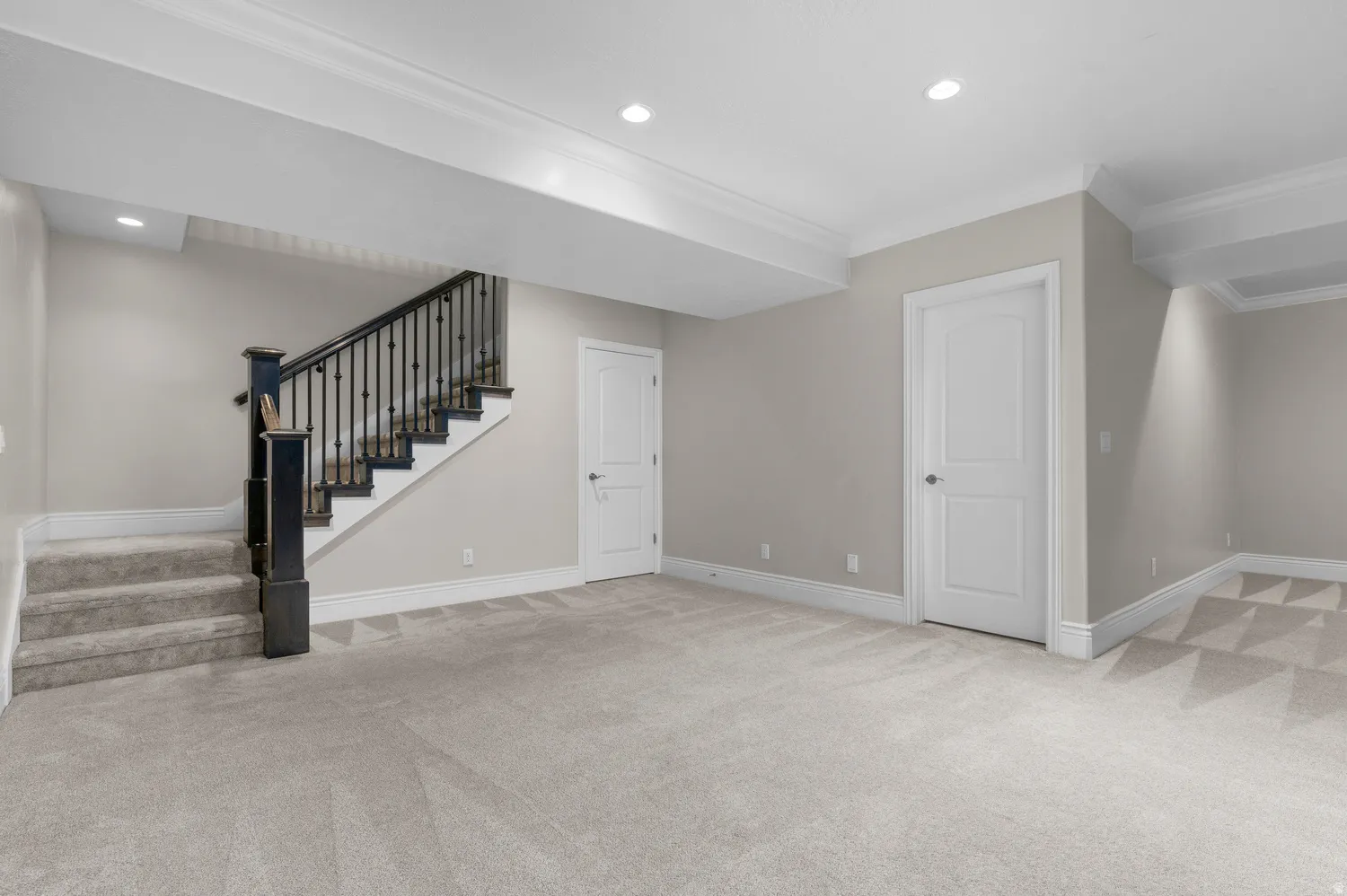 Expansive carpeted area featuring a staircase with dark wood newel posts and railings, recessed lighting, and crown molding