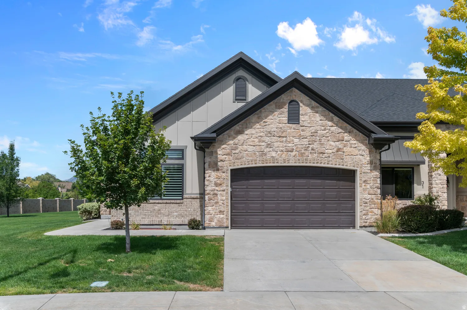 Stone and siding exterior with a two-car garage, dark-toned roof, and a paved driveway