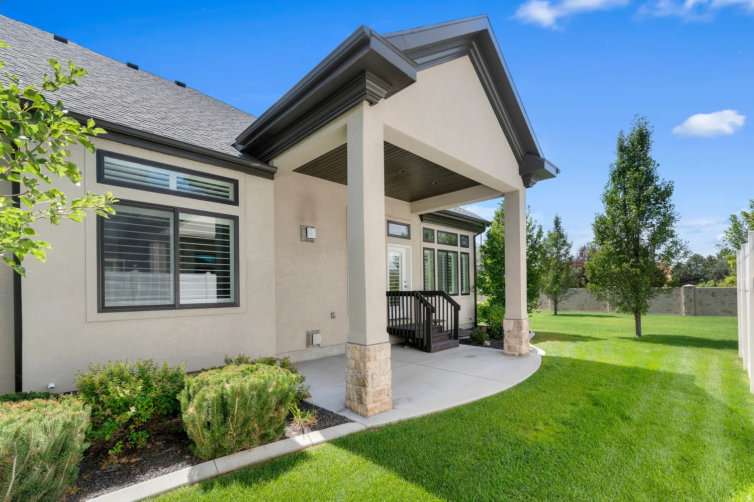 Covered patio with stone-wrapped columns, concrete hardscaping, and a dark wood-finish railing