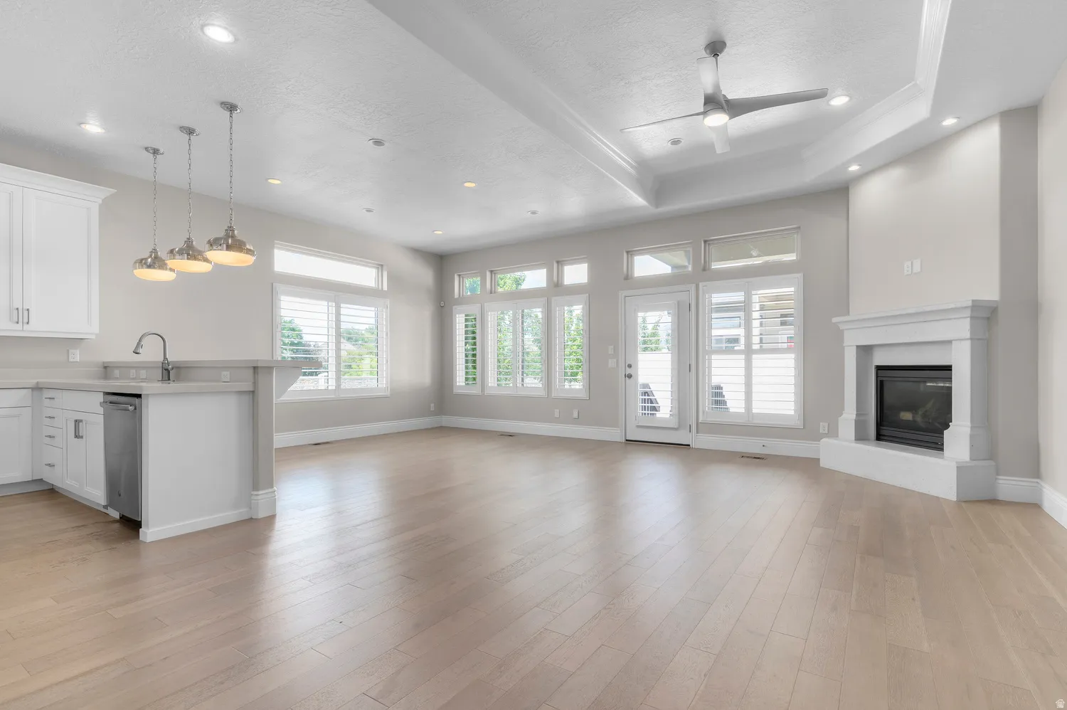 Recessed lighting, wood-finish flooring, white kitchen cabinetry, stainless steel dishwasher, and a built-in fireplace