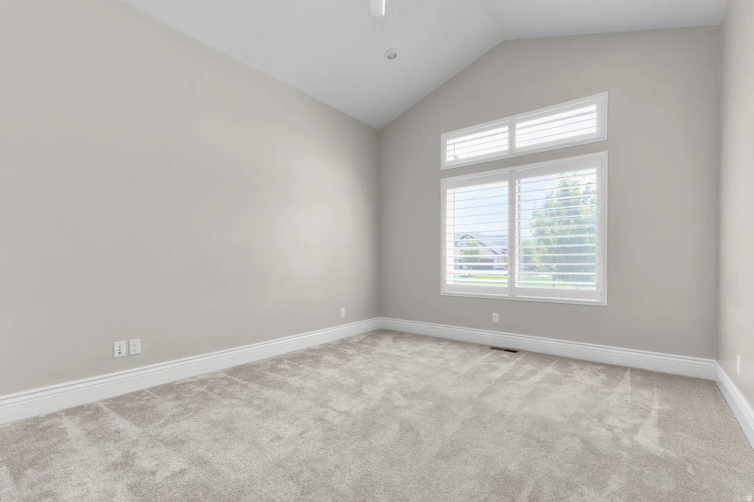 Vaulted ceiling, light neutral wall paint, carpeted flooring, large window with white plantation shutters, recessed lighting