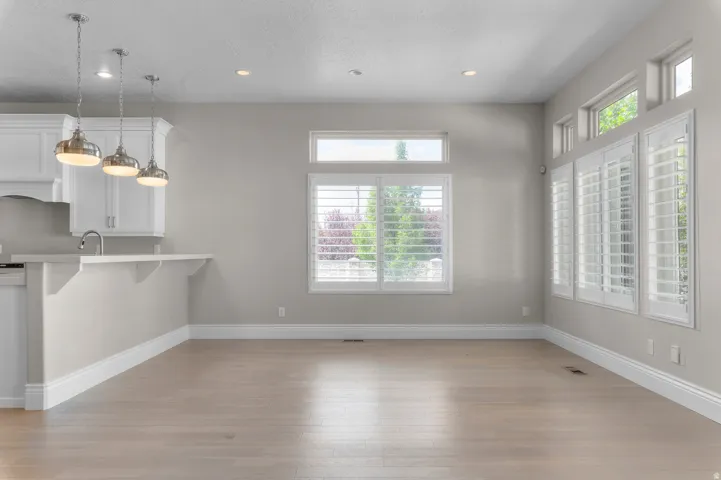 Light wood-finish flooring with white baseboards, kitchen island with seating, white cabinetry, recessed lighting, and multiple windows with white plantation shutters