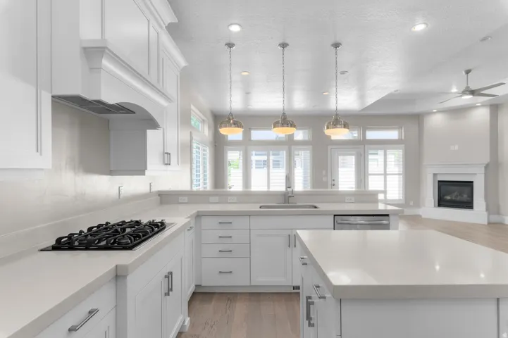 White shaker cabinetry, light countertops, wood-finish flooring, built-in gas cooktop, and a built-in fireplace