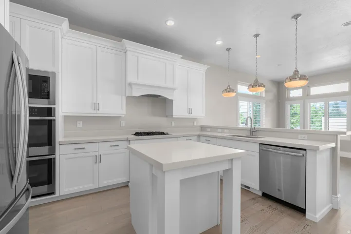 White shaker cabinetry with crown molding, light-toned countertops, a central island, stainless steel appliances, and wood-finish flooring