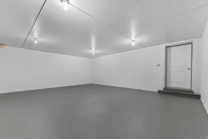 Spacious room featuring a smooth gray floor, white concrete walls, and multiple ceiling-mounted light fixtures