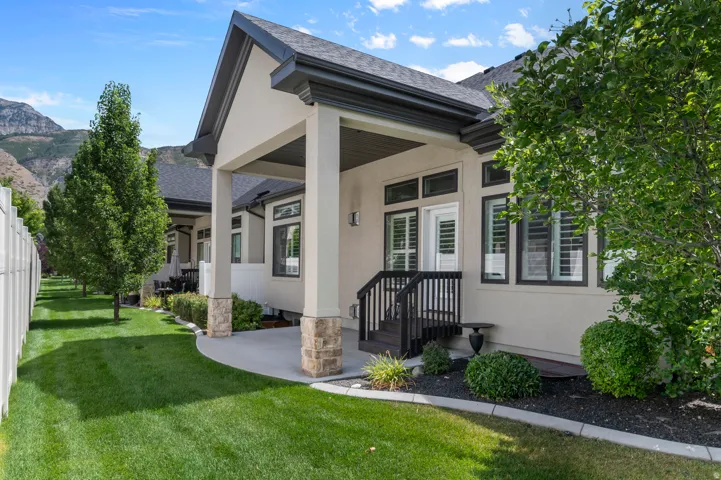 Covered patio with stacked stone pillar bases, dark wood-finish railing, and surrounding landscaping