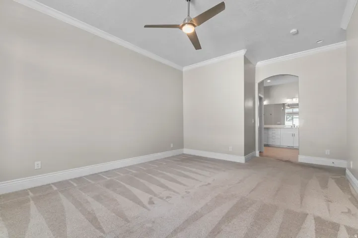 Spacious room with crown molding, textured ceiling, a ceiling fan, and arched entryway