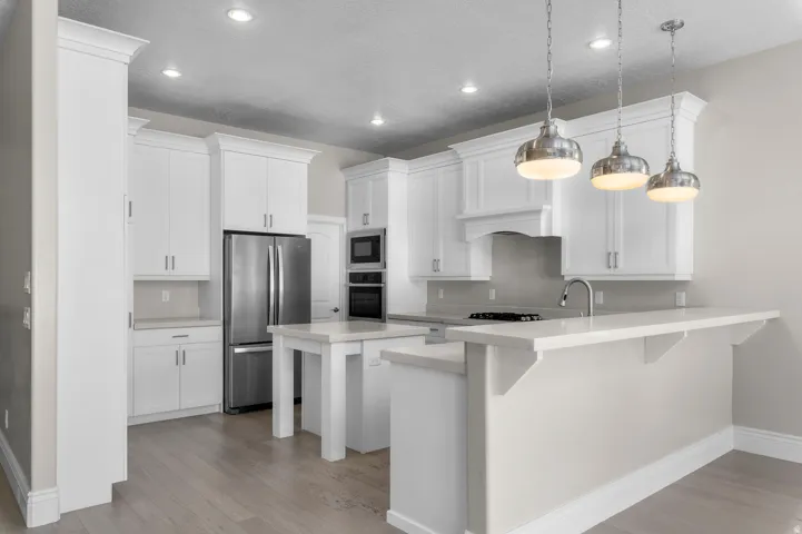 White shaker cabinetry, stainless steel appliances, light wood-finish flooring, recessed lighting, and a kitchen island with pendant lighting