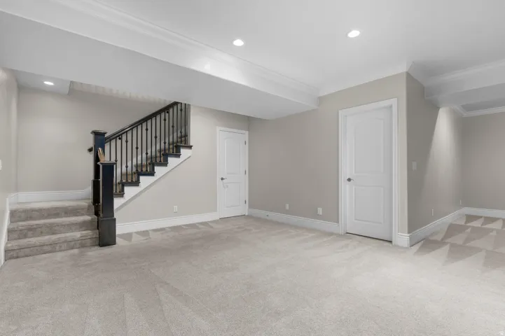 Expansive carpeted area featuring a staircase with dark wood newel posts and railings, recessed lighting, and crown molding