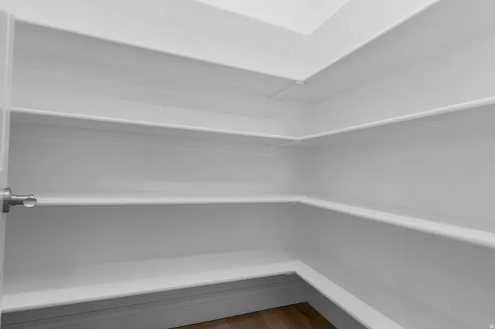Spacious pantry featuring multiple tiers of built-in shelving, white finishes, and wood-finish flooring