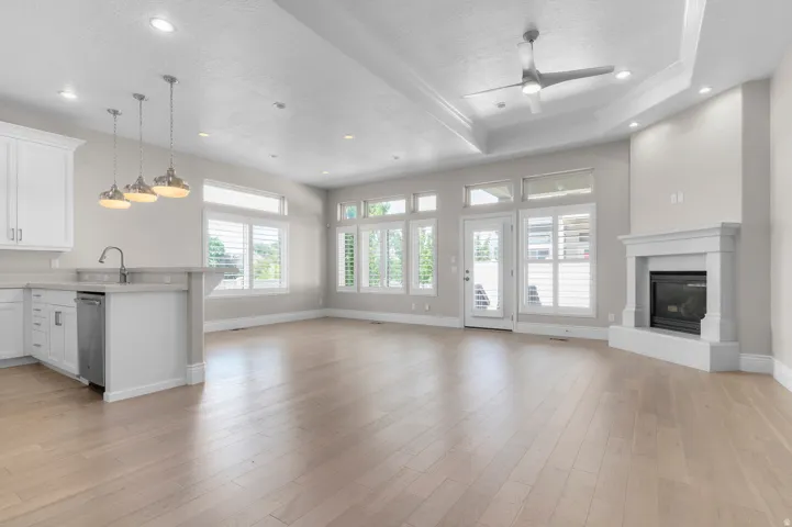 Recessed lighting, wood-finish flooring, white kitchen cabinetry, stainless steel dishwasher, and a built-in fireplace