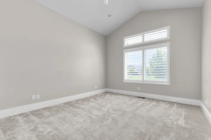 Vaulted ceiling, light neutral wall paint, carpeted flooring, large window with white plantation shutters, recessed lighting