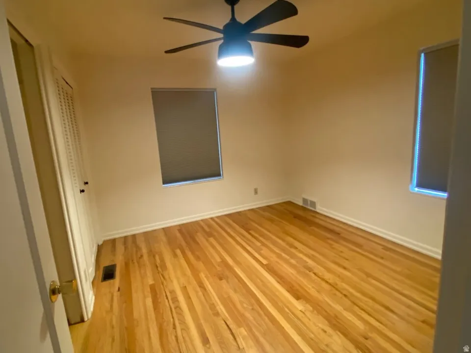 Hardwood flooring, ceiling fan with integrated lighting, two windows, and a louvered closet door. Bedroom 2 on main floor.