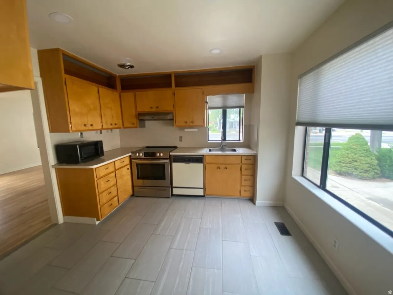 Kitchen featuring wood cabinetry, stainless steel range, a built-in dishwasher, and light-toned tile flooring