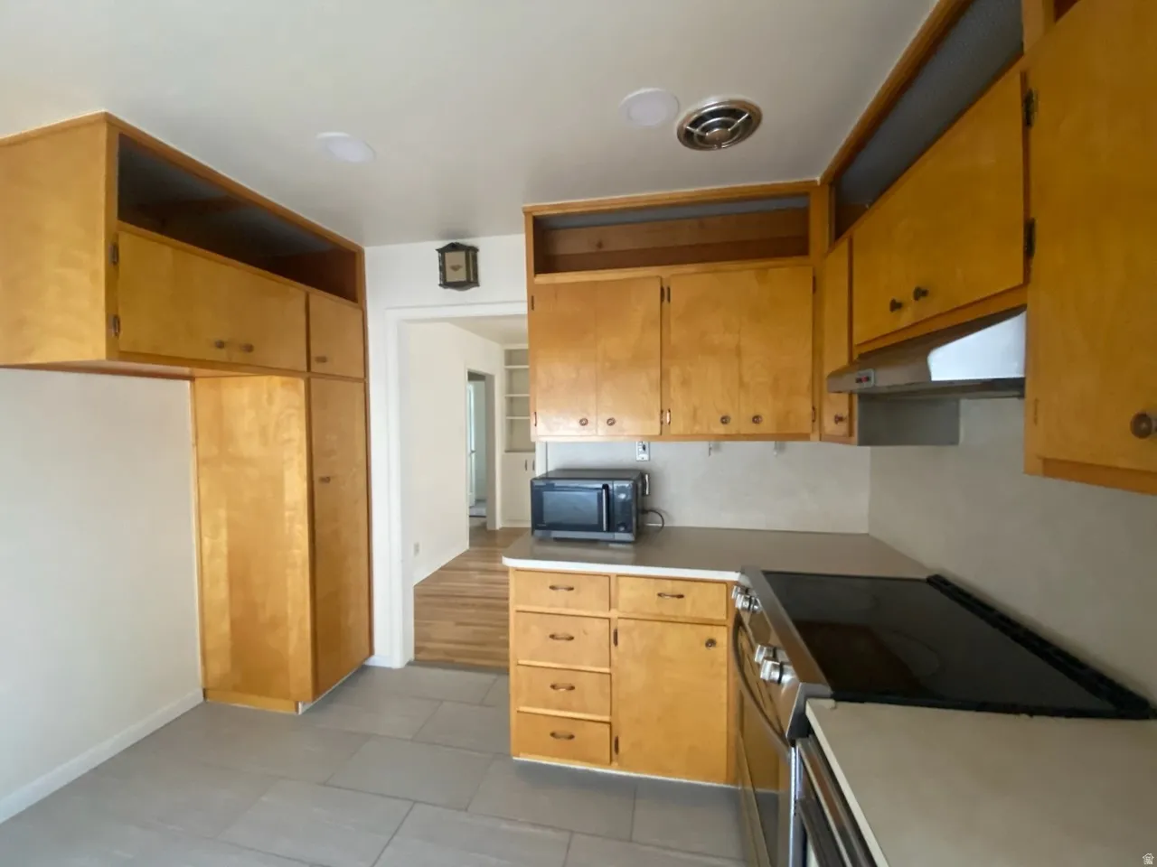 Wood-finish cabinetry, tile flooring, recessed lighting, and a built-in range