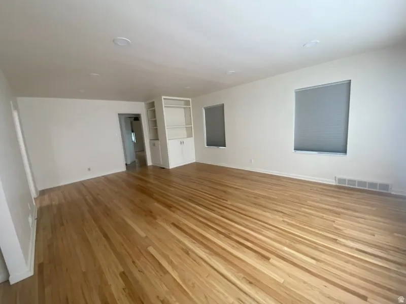 Bright interior with wood-finish flooring, two windows with blinds, recessed lighting, and built-in shelving with lower cabinetry
