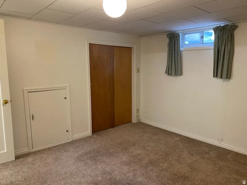 Carpeted room featuring a drop ceiling, closet with wood-finish sliding doors, and window.  Basement bedroom with large closet.