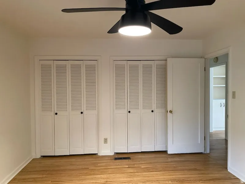 Wood-finish flooring with dual louvered bi-fold closet doors, a ceiling fan with integrated lighting, and white interior doors. Bedroom 2 on main floor.