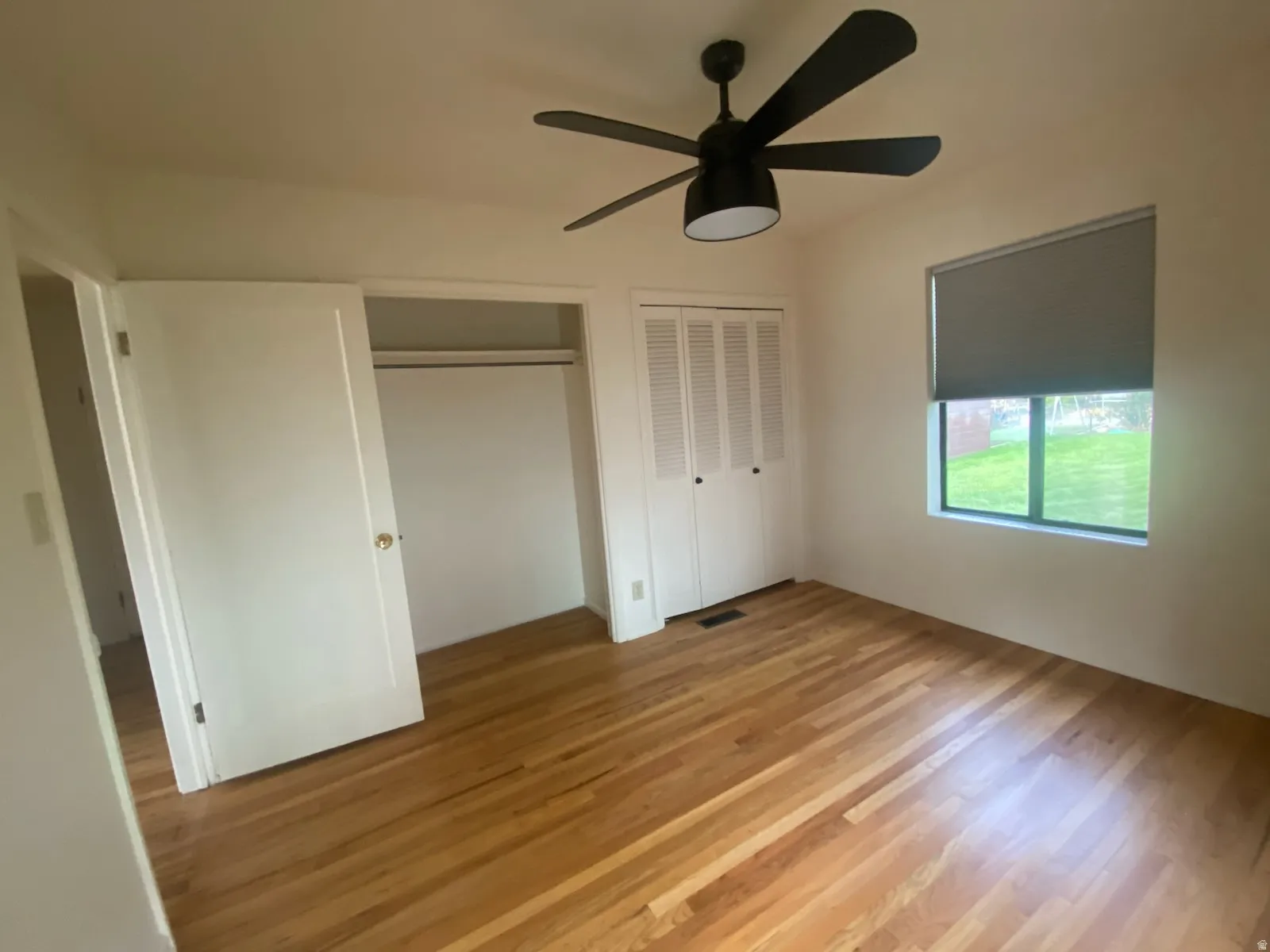 Hardwood flooring, a ceiling fan with integrated lighting, a window with a roller shade, and a closet with bifold doors. Bedroom 1 on main floor.