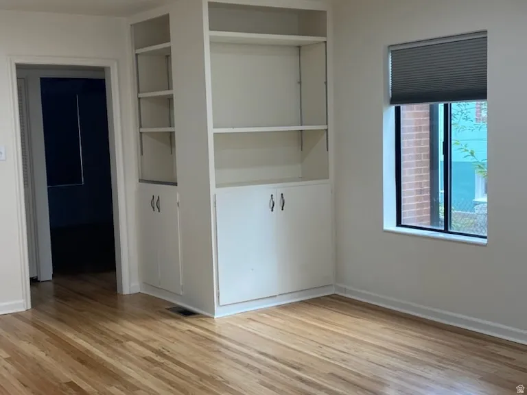 Hardwood flooring, recessed lighting, built-in shelving, white cabinetry, and a window with blinds