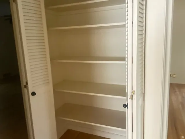 White louvered bifold doors opening to a hall  closet with multiple shelves, over wood-finish flooring.