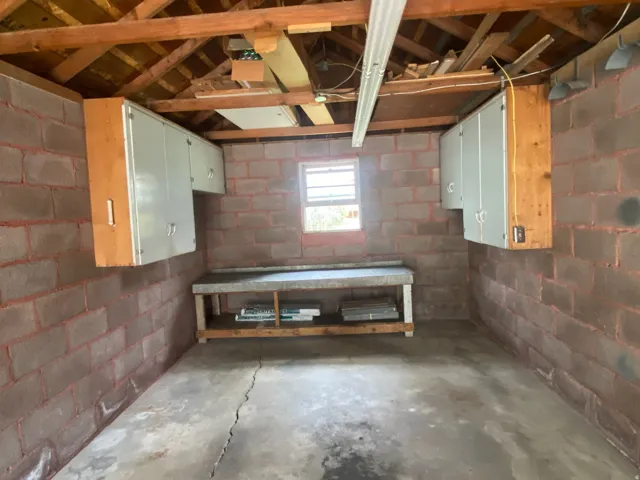 Exposed wood beam ceiling, concrete block walls, built-in storage cabinets, window for natural light, and a built-in workbench