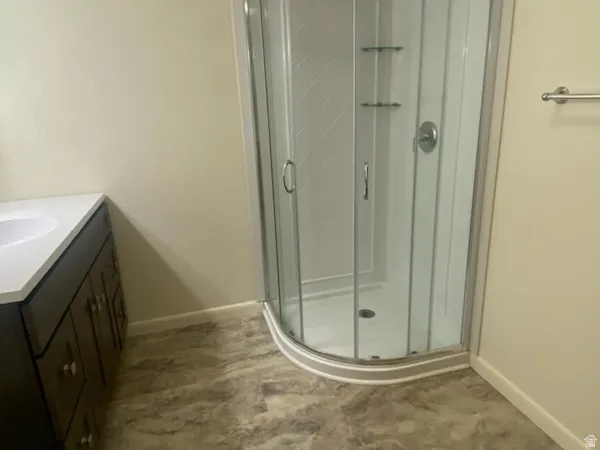 Curved glass shower enclosure with integrated shelving, dark wood-finish vanity with a white countertop, and patterned flooring