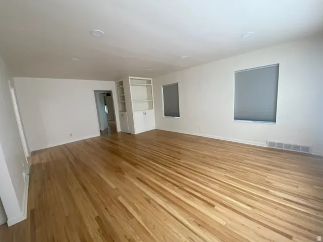 Bright interior with wood-finish flooring, two windows with blinds, recessed lighting, and built-in shelving with lower cabinetry