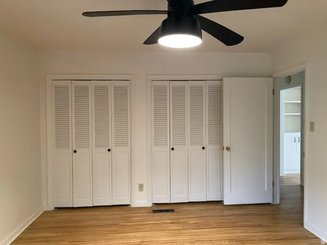 Wood-finish flooring with dual louvered bi-fold closet doors, a ceiling fan with integrated lighting, and white interior doors. Bedroom 2 on main floor.