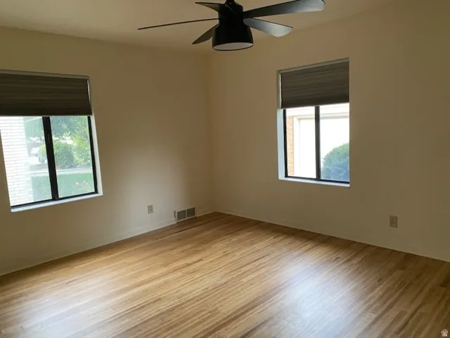 Wood-finish flooring with dual windows featuring blinds and a ceiling fan