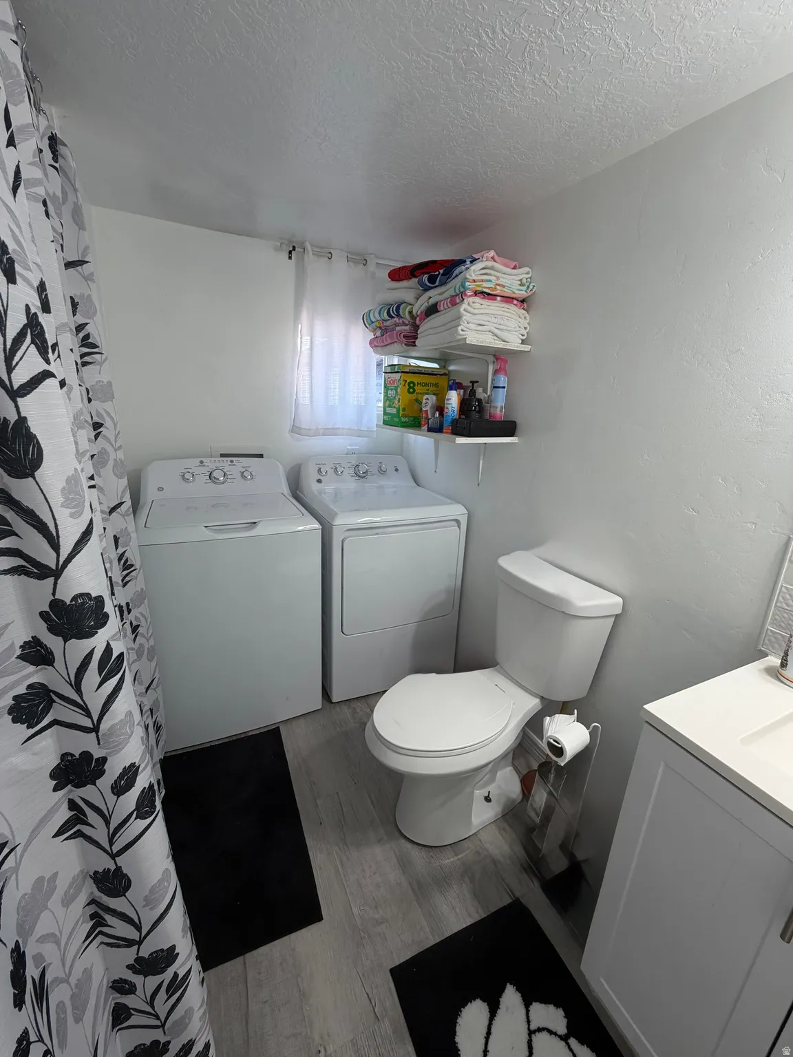 Integrated laundry appliances and toilet with a white vanity and sink, set on wood-finish flooring