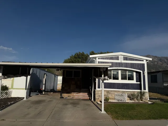 Exterior featuring blue siding, white trim, stone accents, multiple windows, and an attached carport
